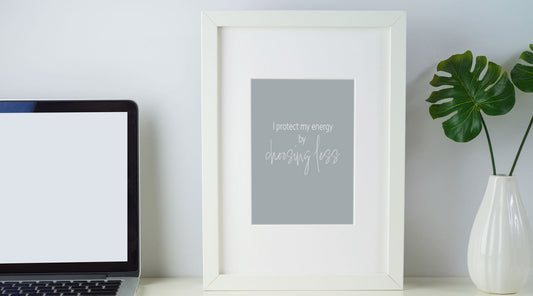Minimalist desk setup with a 5x7 framed affirmation print that reads ‘I protect my energy by choosing less.